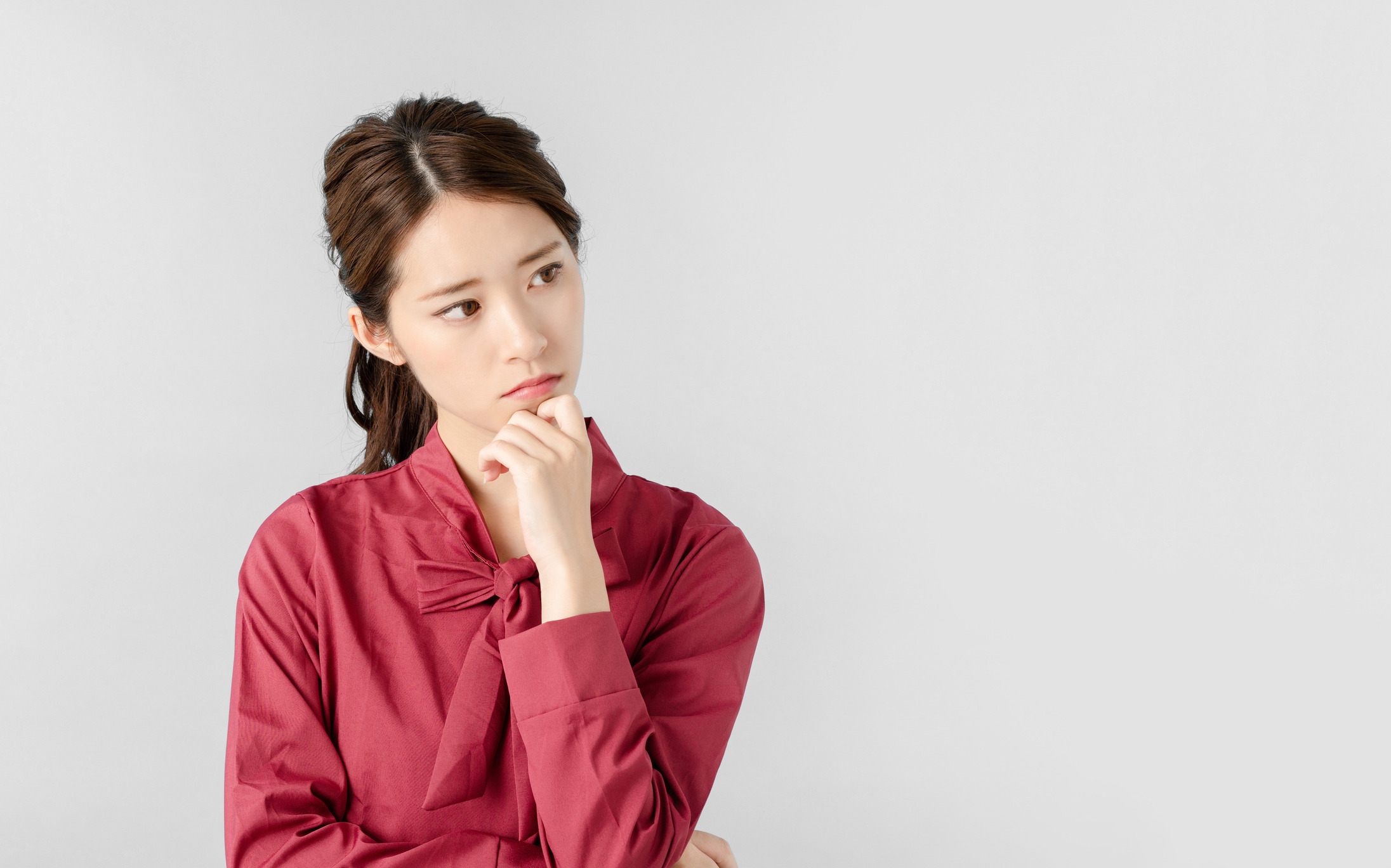 Woman thoughtfully considering options for an aesthetic clinic in Singapore, wearing a red blouse against a light background.
