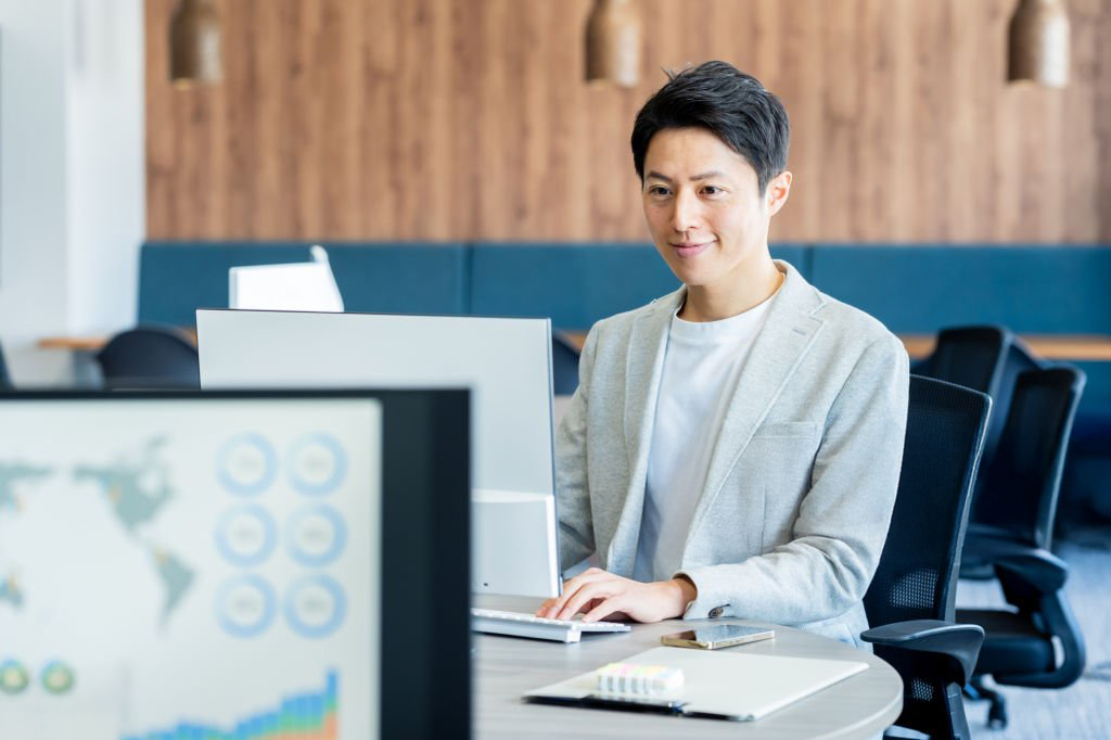 Professional man in a modern office working at a computer, with a Hydrafacial treatment brochure and marketing data visible on the desk.