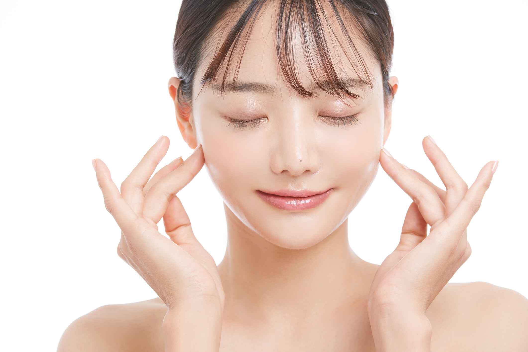 A woman with radiant skin gently touching her cheeks and smiling with closed eyes, showcasing the effects of a skin booster treatment.
