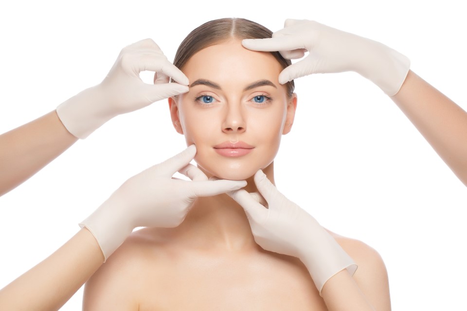 Woman's face being examined by gloved hands, representing facial assessment for Face Lifting Treatment vs. Surgical Facelift.