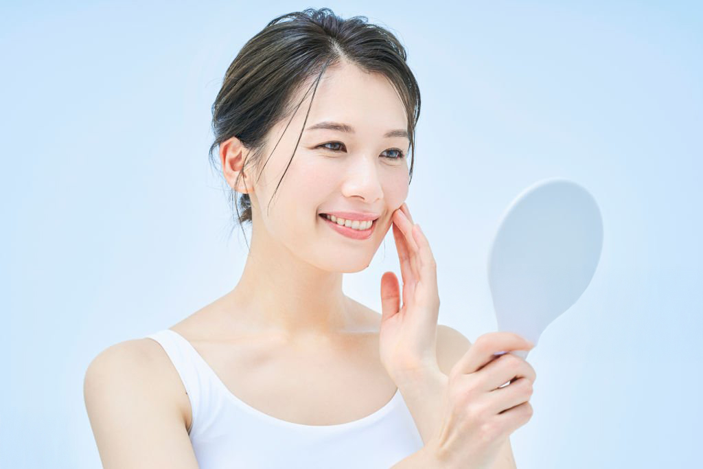 Smiling woman examining her clear skin in a mirror, symbolizing good skin health and skincare routine