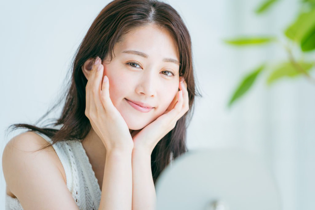 Woman cupping her cheeks and smiling, appreciating the lifted and youthful results of a surgical facelift treatment in Singapore.