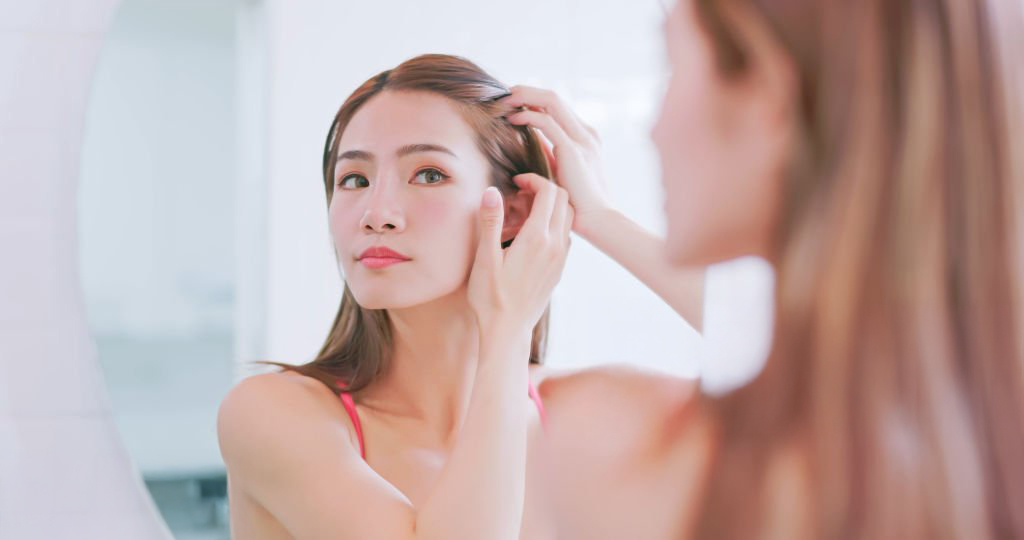 close up asian woman standing in front of mirror is checking her hairline inside bathroom at home