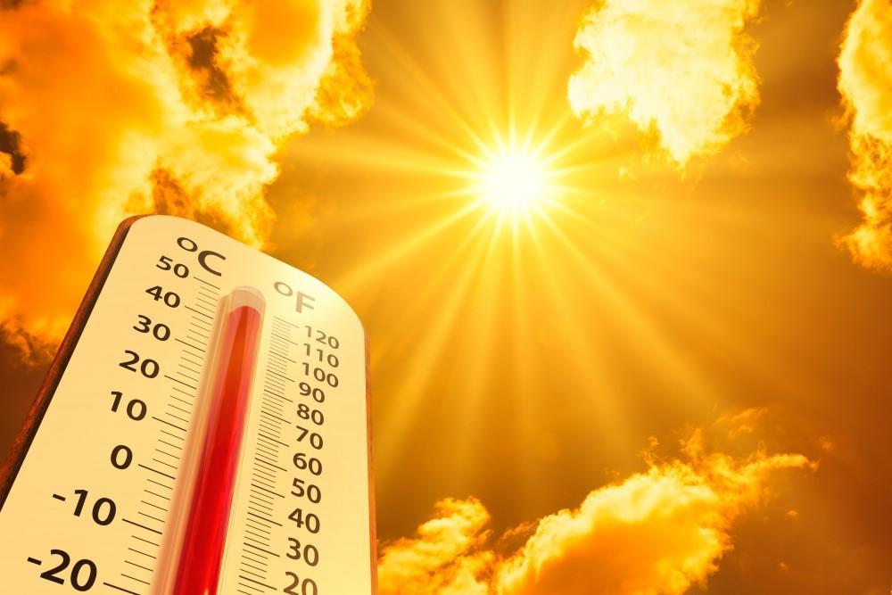 The image depicts a thermometer against a background of a bright, radiating sun and clouds, representing high temperature.
