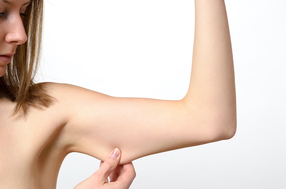 Woman pinching loose skin on her upper arm, illustrating a common concern addressed in guides on how to tighten sagging skin.