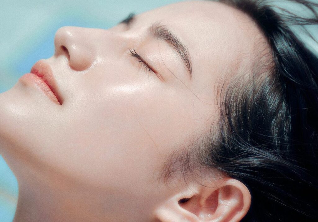 Close-up of a woman with clear glowing skin and closed eyes under sunlight
