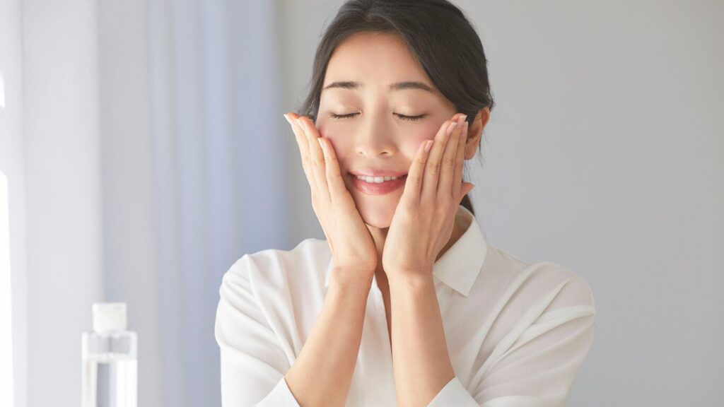 A woman with eyes closed gently applying skincare product to her cheeks to improve hydration