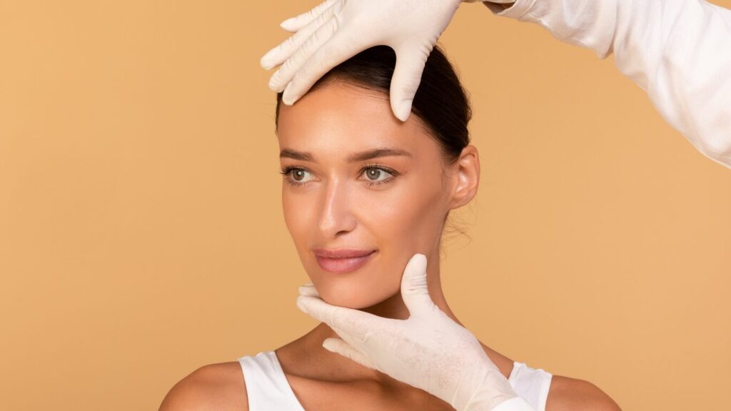 A practitioner in medical gloves assessing a patient's facial structure and skin quality for non-invasive treatment